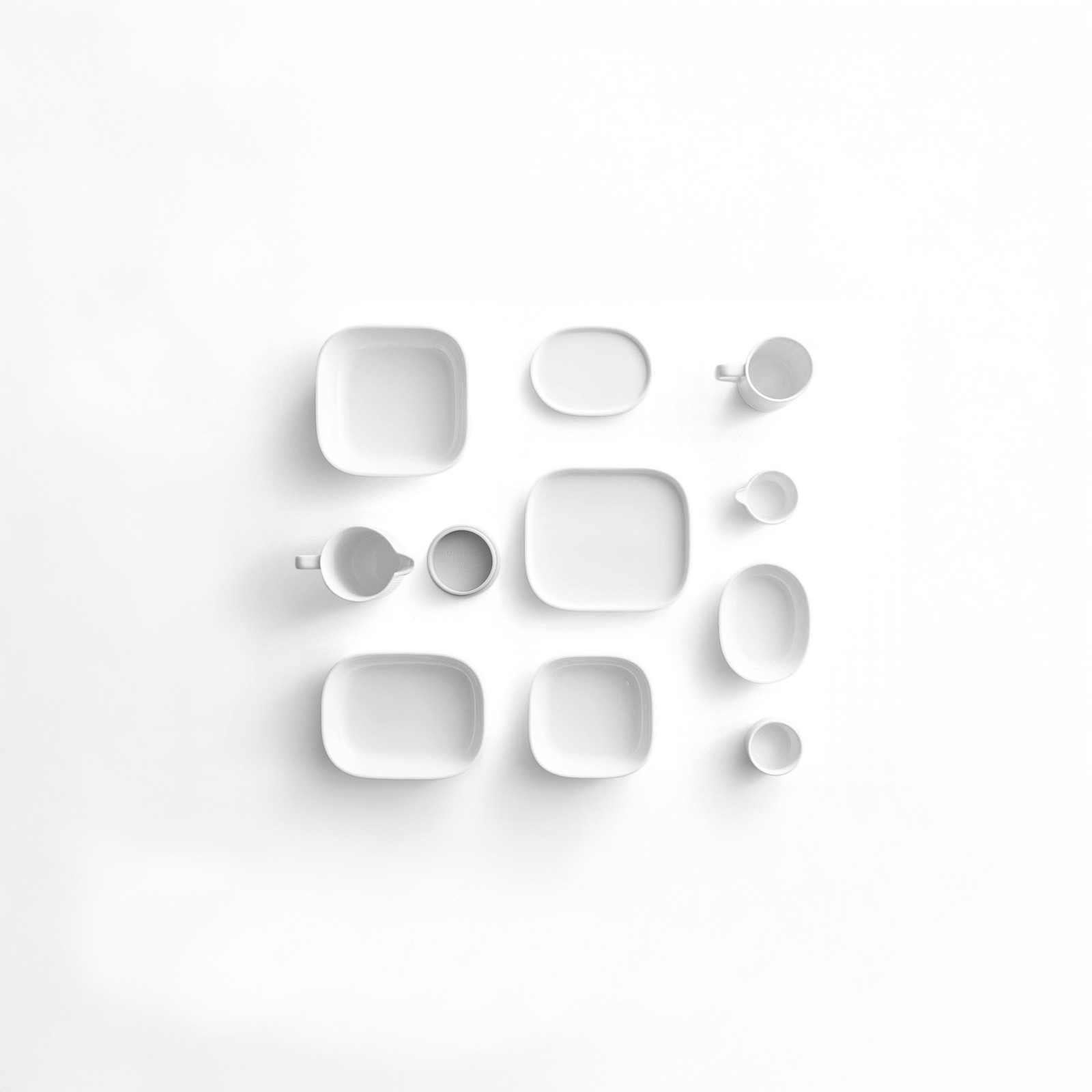 Overhead view of the porcelain group arranged in a grid on a white surface, showing the family of nesting forms.