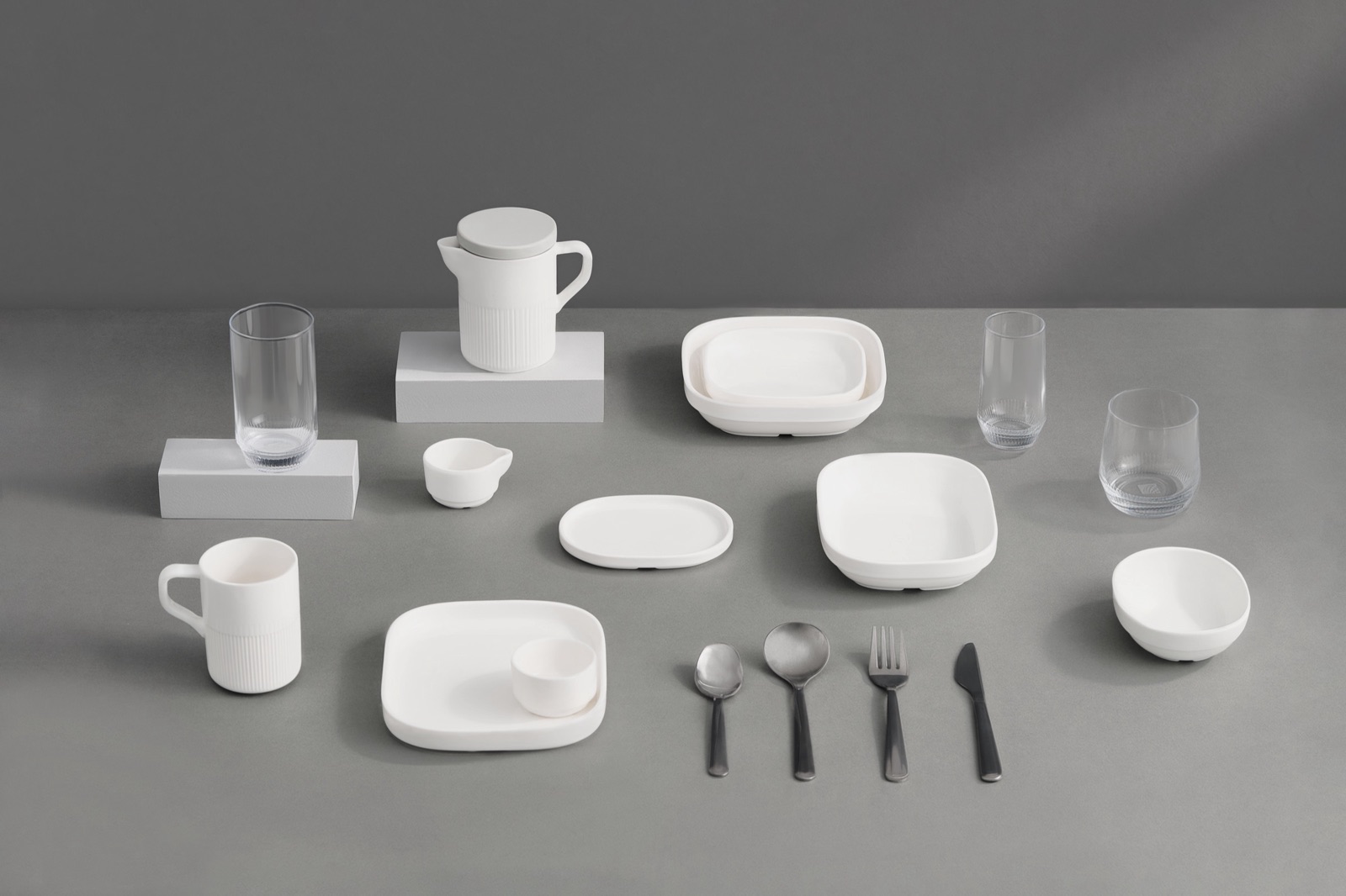 The complete United Airlines premium cabin dinnerware collection - plates, bowls, cups, jug, and cutlery arranged on a grey surface.