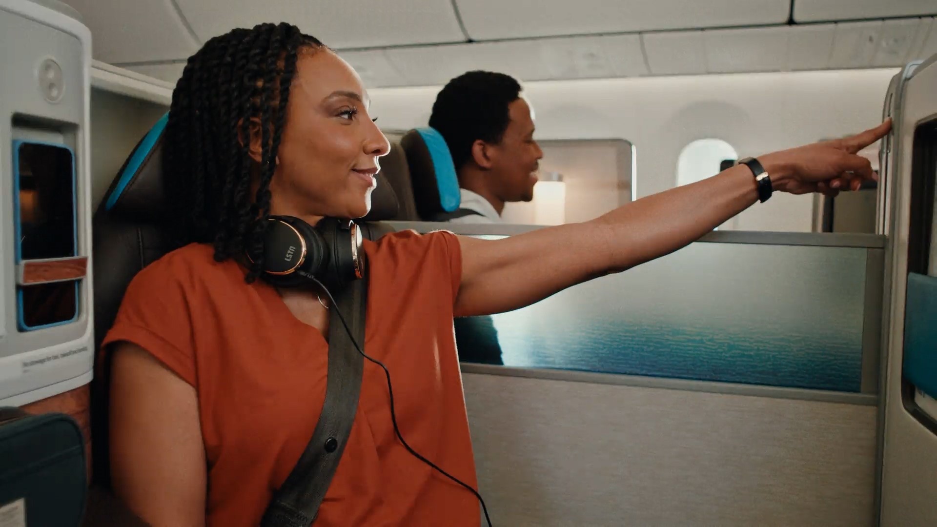 A passenger in an Alaska Airlines Business Class cabin with the headphones resting around her neck, looking out over the ocean.