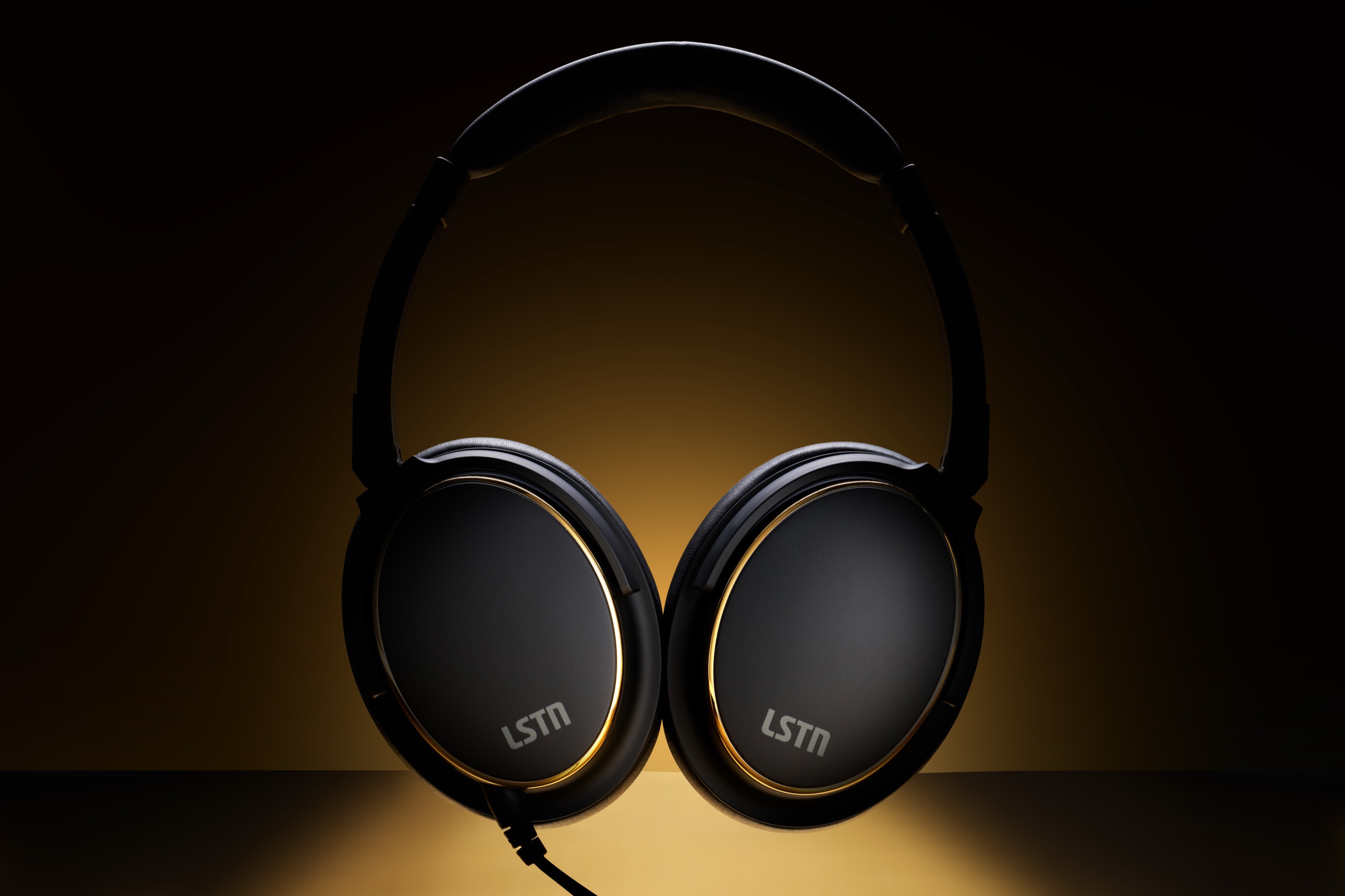 A front view of the LSTN headphones lit in warm gold - matte black earcups ringed in brass with LSTN branding on each cup.