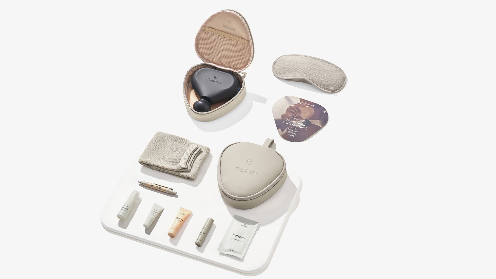The full United x Therabody Premium Plus kit laid out on white - the stone hard-shell pouch, quilted eye mask, Theragun Mini in its case, socks, cleansing towelette, and the custom skincare range.